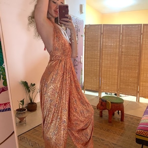 Puede incluir: Un mono holgado con estampado naranja y blanco, escote halter y cierre de nudo en la espalda. El mono está hecho de una tela suave y fluida.