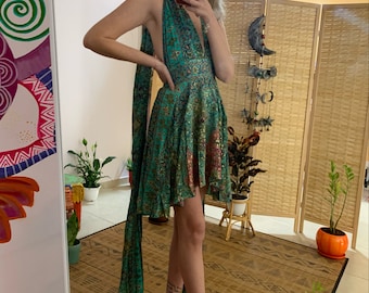 May include: A teal halter dress with a floral pattern and a plunging neckline. The dress has a flowing skirt and long, matching fabric ties. The model is wearing high-heeled sandals. The dress is suitable for a special occasion.