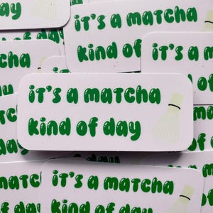 Könnte beinhalten: Ein Satz Aufkleber mit dem Text "It's a matcha kind of day" in grünen Buchstaben auf weißem Hintergrund. Die Aufkleber zeigen eine weiße Schneebesen-Illustration.