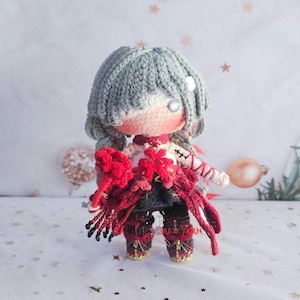 May include: A crocheted doll with light gray hair, a single silver eye, and a pale complexion. The doll wears a white top with red accents, black pants, and red boots. It holds a red floral accessory and features red and black layered clothing.
