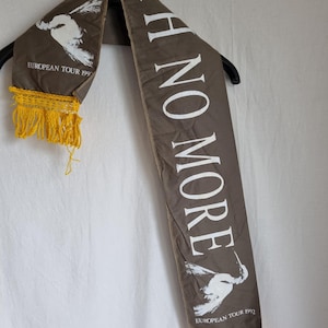 Puede incluir: Una bufanda de tela marr&oacute;n con texto blanco que dice "I H NO MORE" y un gr&aacute;fico de p&aacute;jaro blanco. La bufanda tiene flecos amarillos en ambos extremos y el texto "EUROPEAN TOUR 1992" est&aacute; impreso en ambos extremos.