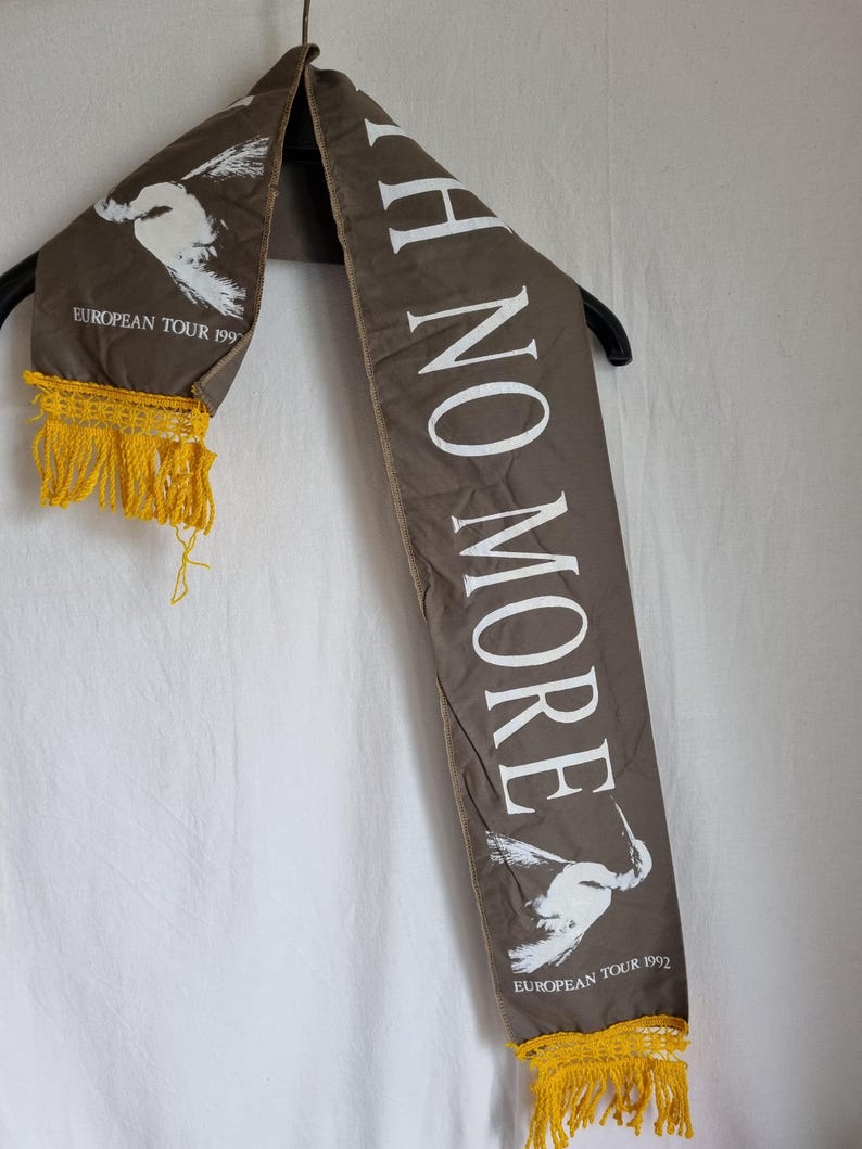 Puede incluir: Una bufanda de tela marr&oacute;n con texto blanco que dice "I H NO MORE" y un gr&aacute;fico de p&aacute;jaro blanco. La bufanda tiene flecos amarillos en ambos extremos y el texto "EUROPEAN TOUR 1992" est&aacute; impreso en ambos extremos.