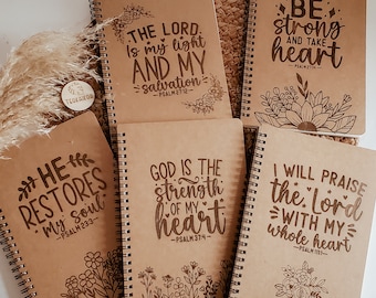 May include: Six brown spiral notebooks with inspirational quotes and bible verses. Each notebook features a different quote and verse, including "The Lord is my light and my salvation", "Be strong and take heart", "He restores my soul", "God is the strength of my heart", "I will praise the Lord with my whole heart".