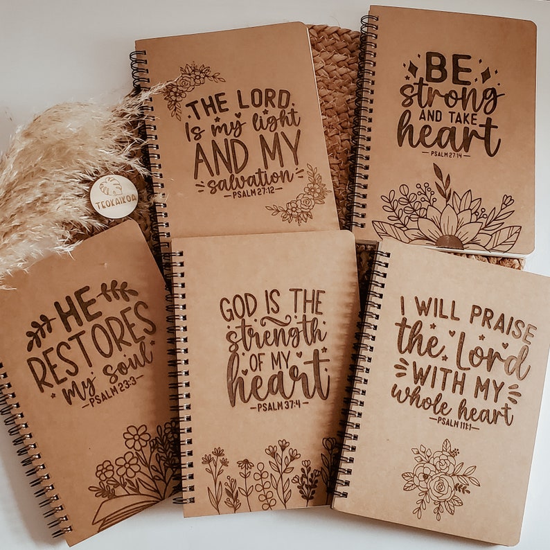May include: Six brown spiral notebooks with inspirational quotes and bible verses. Each notebook features a different quote and verse, including "The Lord is my light and my salvation", "Be strong and take heart", "He restores my soul", "God is the strength of my heart", "I will praise the Lord with my whole heart".