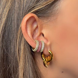 May include: Gold hoop earrings with a layered design. The top layer is a thin hoop with pink and clear rhinestones. The bottom layer is a thicker hoop with a chain link design.