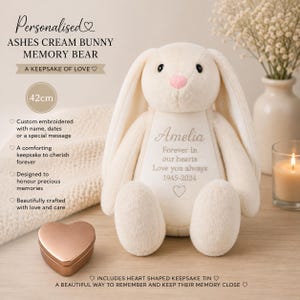 Op de afbeelding: Een crèmekleurige pluche konijnenknuffel met lange oren, een roze neus en zwarte ogen. Op de borst van het konijn zijn de naam Amelia, de tekst Forever in our hearts, Love you always, de data 1945-2024 en een hartsymbool geborduurd.