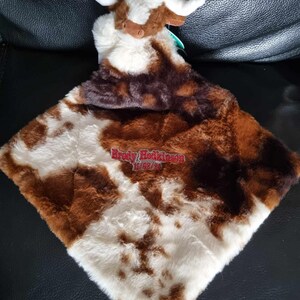 May include: A plush security blanket featuring a soft, brown and white cow head attached to a square, faux-fur blanket with a brown and white cow-print pattern. The blanket is embroidered with the red text Brody Hodkinson and the date 11/08/23.