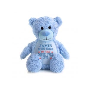 Pode incluir: Um urso de pelúcia azul claro com focinho e barriga azul claro. O urso tem o texto "JAMIE NEWEST MEMBER OF THE TONSIL FREE CLUB" bordado na barriga em azul e vermelho.
