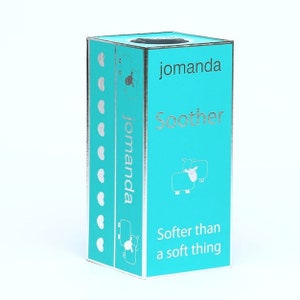 May include: A rectangular turquoise box with silver accents. The front features the text jomanda Soother, a line drawing of a sheep, and the phrase Softer than a soft thing. The side displays the brand name jomanda and a vertical row of silver hearts.