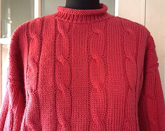 Op de afbeelding: Een rode kabelgebreide trui met een mock neck.