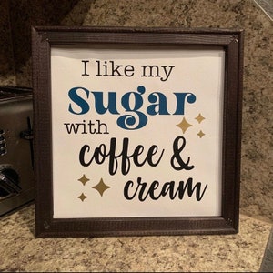 May include: A framed sign with the text "I like my sugar with coffee & cream" in black and blue lettering with gold glitter accents.