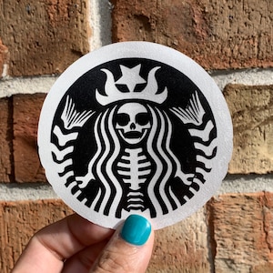 May include: A black and white sticker featuring a skeleton mermaid wearing a crown with a star on top. The mermaid is inside a circle with a black background and white outline.