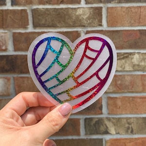 Op de afbeelding: Een hartvormige sticker met een regenboogvleugelontwerp. De sticker heeft een transparante achtergrond met een textuurpatroon. Het vleugelontwerp heeft een kleurengradient, waaronder rood, oranje, geel, groen, blauw en paars.