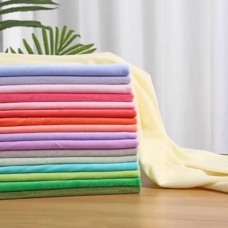 May include: A stack of folded fabric squares in a variety of colors including light yellow, lavender, pink, red, orange, peach, purple, gray, light blue, turquoise, lime green, bright green, and olive green, with a long piece of yellow fabric.