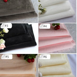 May include: Six samples of fabric in different colors, including gray, white, black, pink, beige, and cream. Each fabric sample is folded and stacked on a white surface. The samples are labeled with numbers 1 through 6.