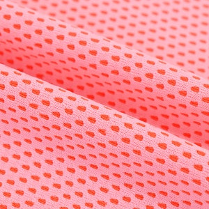 May include: Close-up of a pink fabric with a dotted pattern in a darker shade of red. The fabric is folded, showing the texture and the arrangement of the dots. The material appears to be lightweight and breathable.
