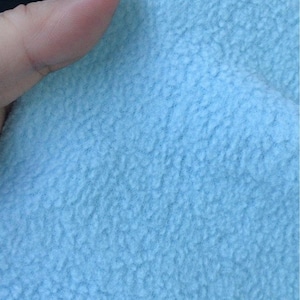 May include: Close-up of a light blue fleece fabric with a soft, fuzzy texture.