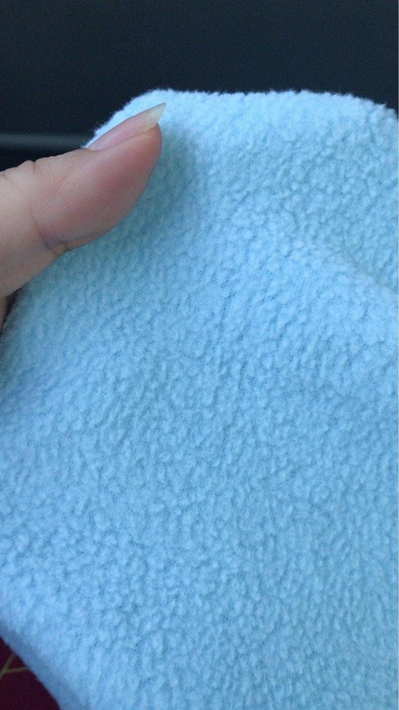 May include: Close-up of a light blue fleece fabric with a soft, fuzzy texture.