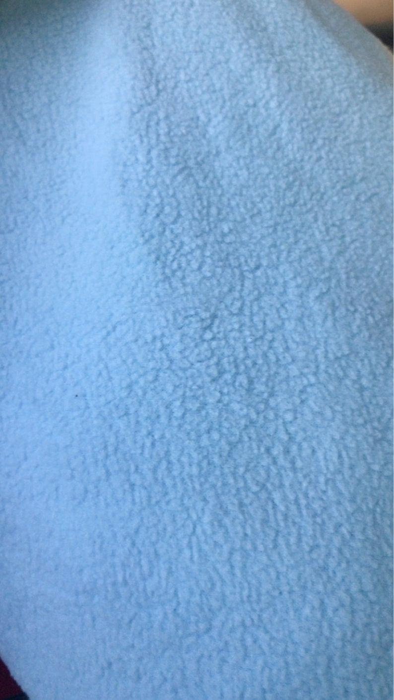 May include: A close-up of a light blue fuzzy fabric. The fabric has a soft, textured surface.