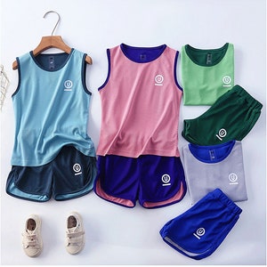 May include: A collection of athletic wear sets in various colors, including blue, pink, green, and gray. Each set features a sleeveless top and matching shorts. The tops and shorts have a mesh design and a white logo. The sets are displayed on a white surface.