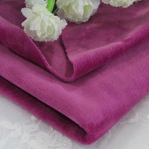 May include: A close-up of a soft, plush fabric in a deep pink hue. The fabric is folded in half, revealing the texture and color of the material.