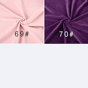 May include: Two swatches of velvet fabric with a soft, plush texture. The left swatch is light pink and labeled 69#. The right swatch is deep purple and labeled 70#. Both fabrics feature gathered folds that create subtle shadows and highlights.