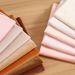 K&ouml;nnte beinhalten: Ein Stapel von 10 verschiedenen farbigen Samtstoffproben. Die Farben sind rosa, beige, braun, orange und dunkelbraun.