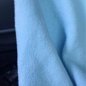 May include: A close-up of a light blue fleece fabric. The fabric has a soft, fuzzy texture.