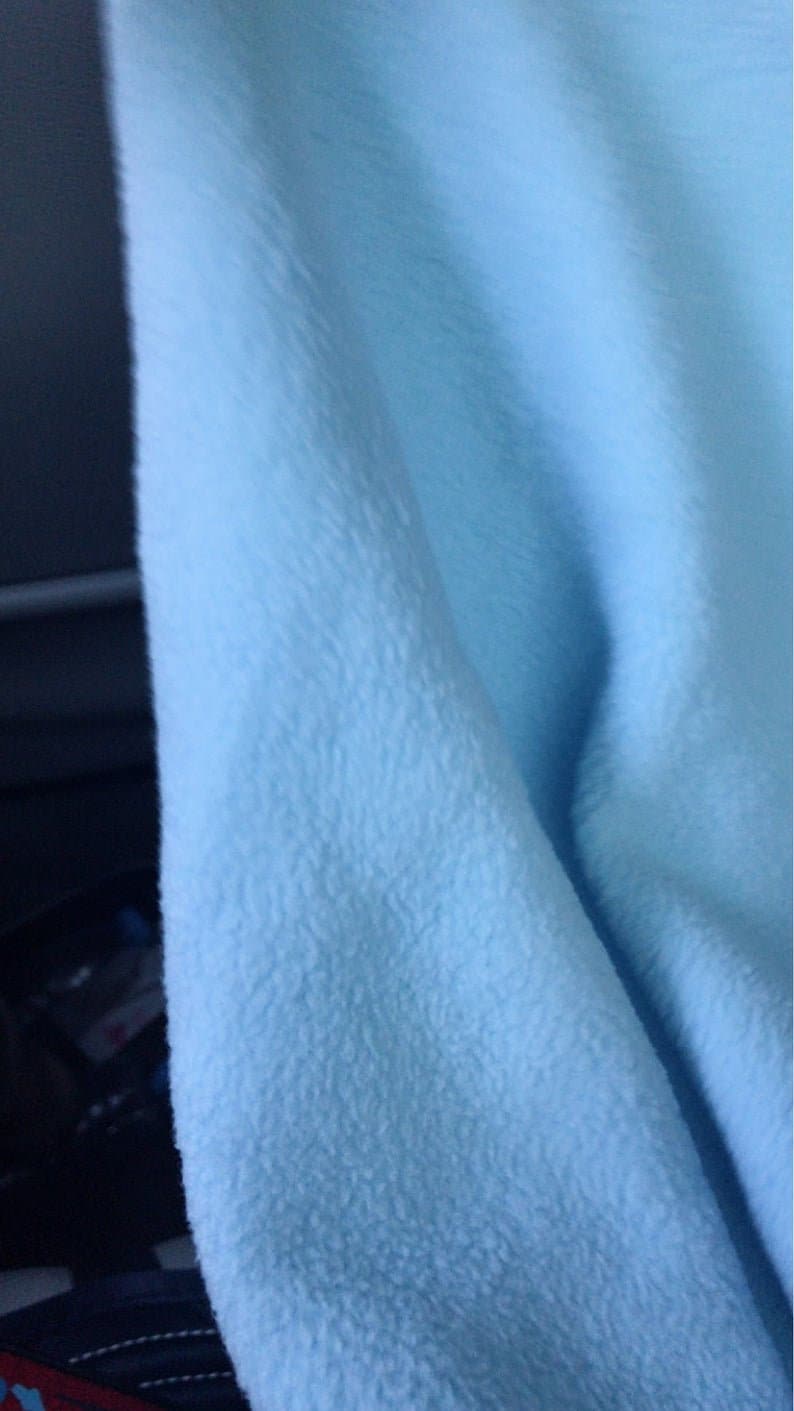 May include: A close-up of a light blue fleece fabric. The fabric has a soft, fuzzy texture.