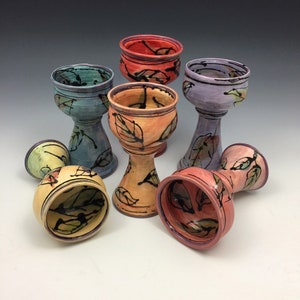 Könnte beinhalten: Sechs Keramikbecher mit einem Blattdesign in verschiedenen Farben, darunter Gelb, Orange, Rot, Lila, Blau und Grün. Die Becher haben einen breiten Boden und eine schmale Oberseite.