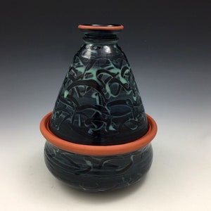 May include: A blue and green ceramic food storage container with a lid. The container has a swirling pattern and a terracotta rim.