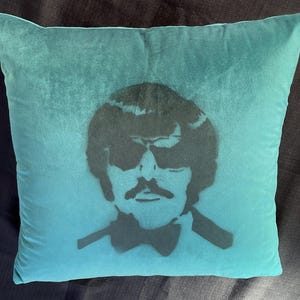 Puede incluir: Una almohada azul turquesa con una plantilla en blanco y negro de una persona con gafas de sol y pajarita.