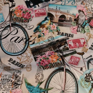 Könnte beinhalten: Cremefarbener Stoff mit einem sich wiederholenden Muster aus Fahrrädern, Pariser Wahrzeichen, Vögeln und Blumenarrangements. Das Wort "Paris" ist in Schreibschrift geschrieben, zusammen mit "Bonjour". Das Design umfasst Briefmarkenillustrationen.