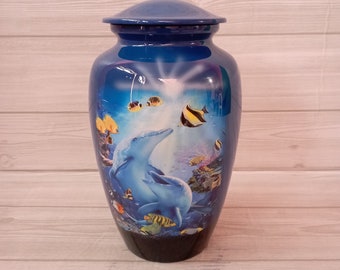 May include: Blue and black ceramic urn with a dolphin and fish design. The urn has a lid and is decorated with a colorful underwater scene.