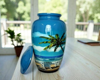 Könnte beinhalten: Blaue Keramikurne mit Strandmotiv. Die Urne zeigt eine Palme, Strandstühle und einen blauen Himmel mit Wolken. Der Deckel liegt neben der Urne auf einer hellen Holzoberfläche.