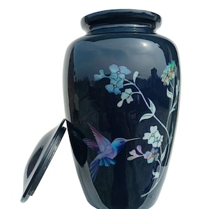 Könnte beinhalten: Eine schwarze Keramikurne mit einem Kolibri- und Blumendesign. Die Urne hat einen Deckel und ist mit Perlmutteinlegearbeiten verziert.