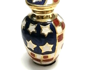 May include: A small, gold-colored urn with a blue, white, and red enamel design. The design resembles the American flag.