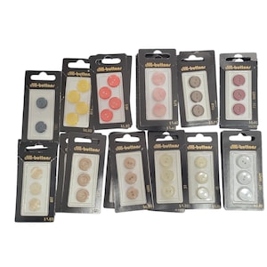May include: Assortment of Dill-buttons in various colors, including yellow, pink, and gray, packaged in black and clear plastic. Each package contains three buttons. The text "dill-buttons" is visible on the packaging.