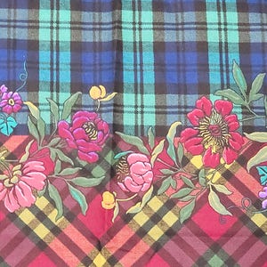 May include: A fabric with a plaid pattern in shades of blue, green, and burgundy. The bottom edge features a floral design with pink and purple flowers, green leaves, and yellow accents. The overall design is a mix of classic and floral elements.