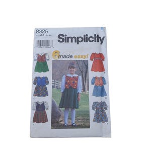 May include: A Simplicity 8325 sewing pattern envelope for children's dresses in sizes 3, 4, 5, and 6. The front features the text 'Simplicity' and 'made easy!' with illustrations of six different dress variations, including solid and patterned fabrics.