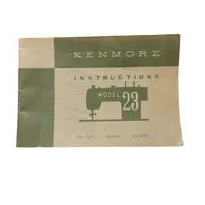 Puede incluir: Un manual de instrucciones vintage para una máquina de coser Kenmore modelo 23 de zigzag. La portada es beige con detalles verdes y presenta una ilustración en blanco y negro de la máquina.