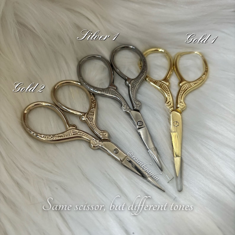 May include: Three pairs of decorative scissors in gold and silver tones. The scissors have an ornate design and are labeled "Gold 1", "Gold 2", and "Silver 1". The text "Same scissor, but different tones" is also visible.