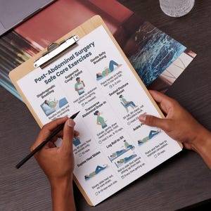 May include: A wooden clipboard with a printed guide titled "Post-Abdominal Surgery Safe Core Exercises" is held by a person. The guide features illustrations and instructions for various exercises, including breathing techniques and stretches. A pen is held over the guide.