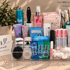 May include: A collection of personal care items including Rave hairspray, lavender hand cream, makeup remover wipes, dental floss, Band-Aids, Shout wipes, Orbit gum, hair ties, and mints. A sign reads: ladies help yourself compliments of the newlyweds.