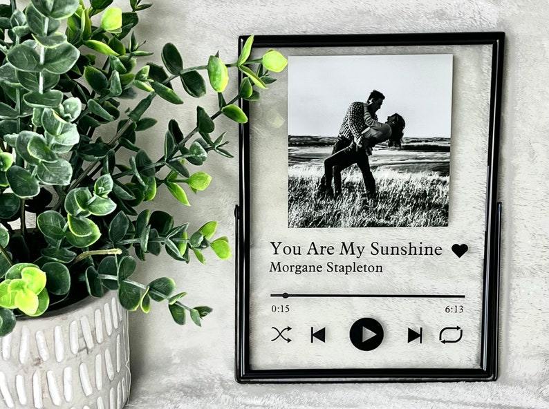 May include: Black framed photo with a black and white photo of a couple dancing on a beach. The photo is displayed in a music player style frame with the song title "You Are My Sunshine" by Morgane Stapleton and play, pause, and skip buttons.