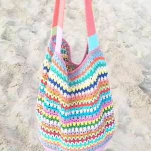 May include: A colorful crocheted tote bag with rainbow stripes and white bobbles. The bag has pink straps.