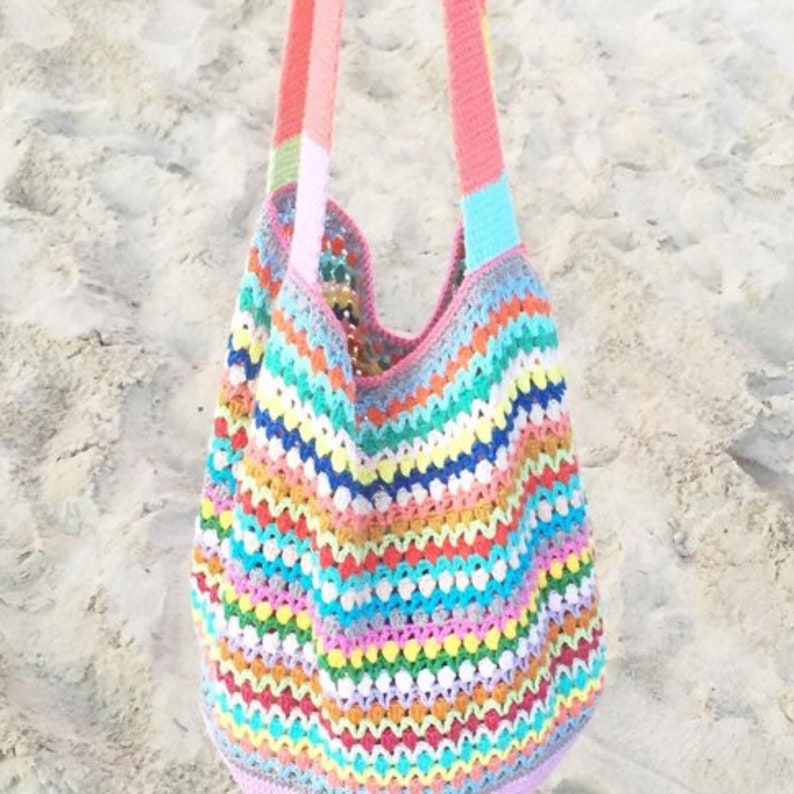 May include: A colorful crocheted tote bag with rainbow stripes and white bobbles. The bag has pink straps.