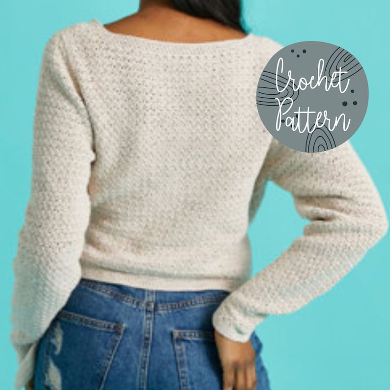 Pu&ograve; includere: Un primo piano di un maglione bianco all'uncinetto con scollo a V e maniche lunghe. Il maglione &egrave; indossato da una persona con jeans blu. Il testo "Crochet Pattern" &egrave; scritto in un cerchio sull'immagine.