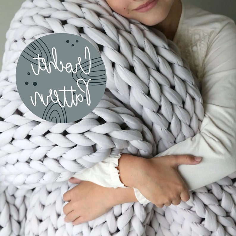 May include: A person holding a large, chunky knit blanket made of thick, white yarn. The blanket is soft and fluffy, and the person is holding it close to their body. The blanket is a popular choice for home decor and can be used as a throw or a bedspread.