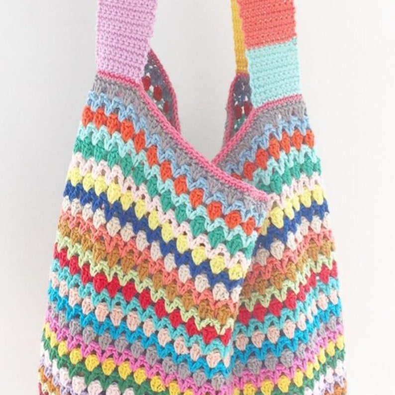 May include: A colorful crocheted tote bag with a rainbow striped pattern. The bag has two straps and is made with a variety of different colored yarns.